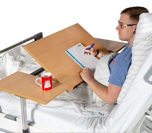 Patient im Pflegebett arbeitet am Brücken-Betttisch mit geneigter Tischplatte